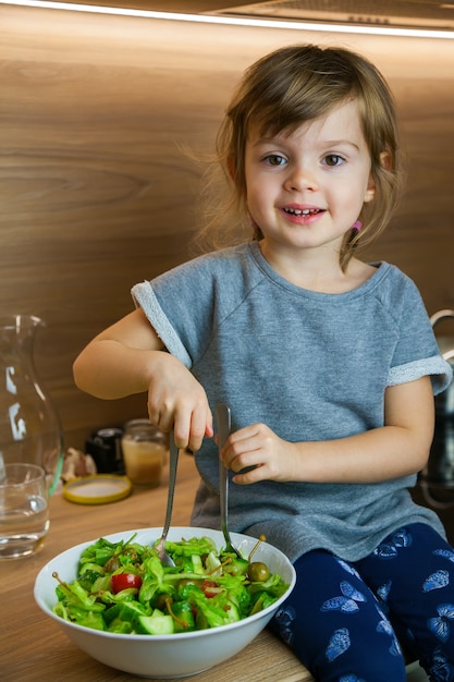 Lächelndes kleines Mädchen, das einfachen grünen Gemüsesalat kocht.