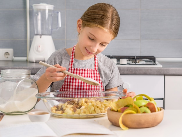 Lächelndes kleines Mädchen, das Zucker zur Srudelapfelfüllung hinzufügt