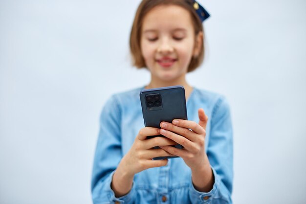 Lächelndes kleines Mädchen im lässigen Jeanskleid hält Smartphone