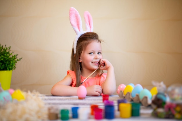 Lächelndes kleines Mädchen in Hasenohren bereitet sich auf Ostern vor bemalte Ostereier fröhliches Osterkonzept