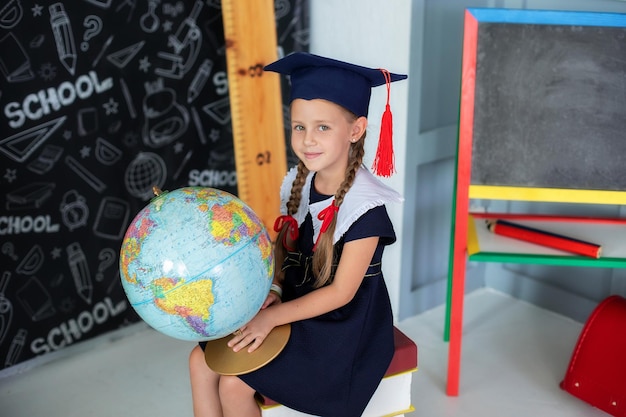 Lächelndes kleines Mädchen in Schuluniform und Zöpfen mit Globus im Klassenzimmer.