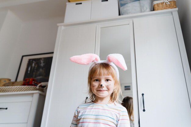 Lächelndes kleines Mädchen mit bemaltem Gesicht und Kaninchenohren am Osterdag