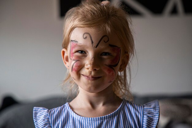 Foto lächelndes kleines mädchen mit gesichtsbemalung und aufgemaltem schmetterlingsgesicht