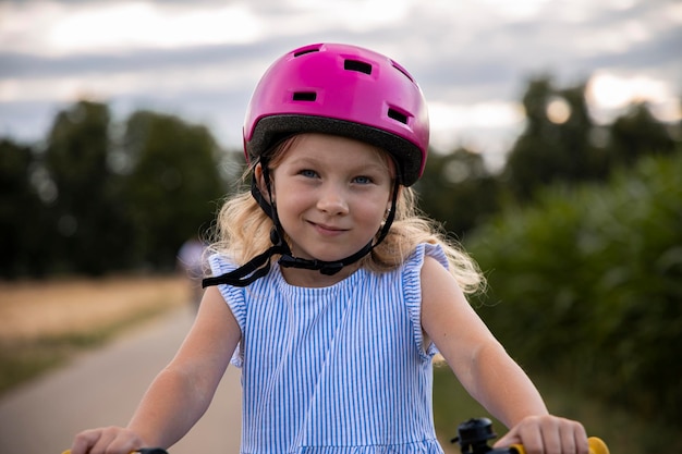 Lächelndes kleines Mädchen mit Helm und Fahrrad auf dem Hintergrund des Feldes