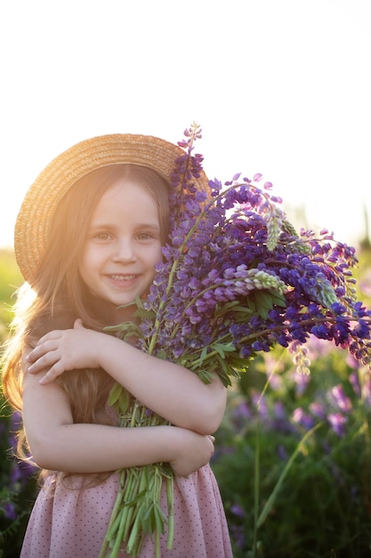 Lächelndes kleines Mädchen mit Lupinenstrauß Ein Kindermädchen in einem Lupinenfeld auf der Sommerwiese