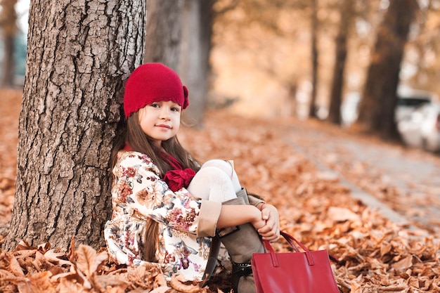 Lächelndes kleines Mädchen mit stylischer Jacke, Strickmütze und Tasche im Freien