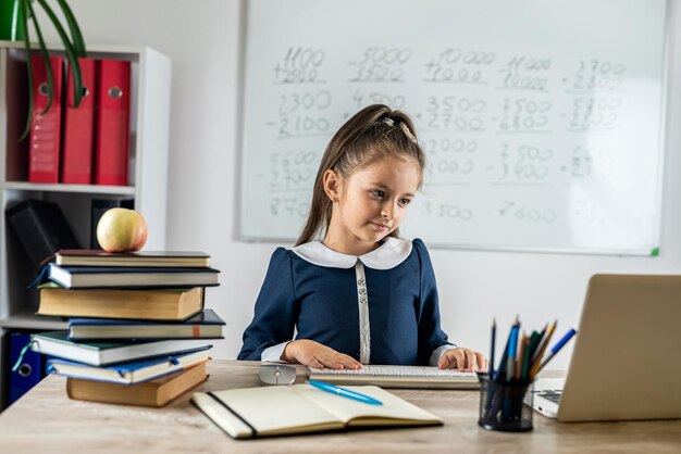 Lächelndes kleines Schulmädchen, das sich Notizen macht und sitzt und in die Kamera schaut Lernkonzept Bildung