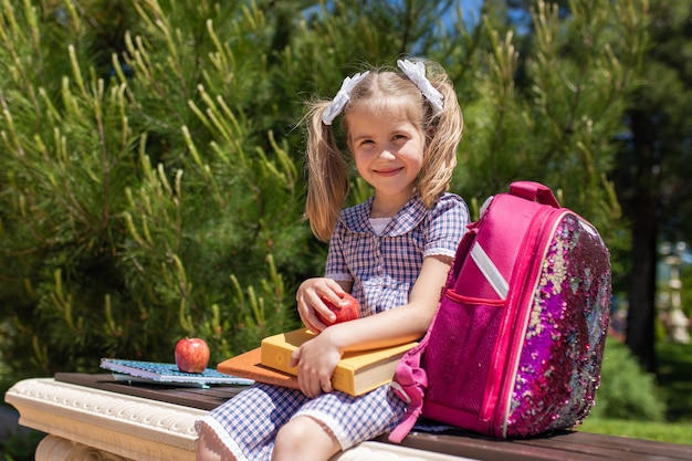 Lächelndes kleines süßes schulmädchen in uniform mit schultaschenrucksack zurück zur schule am 1. september