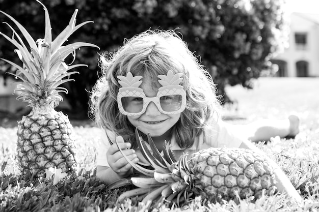 Lächelndes lustiges Kind mit Ananas-Sonnenbrille im Freien Sommerkindjunge im verrückten Ananas-Stil lustig s