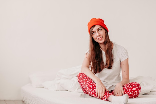 Foto lächelndes lustiges mädchen mit rotem hut und weihnachtspyjamas sitzt mit weißen laken im bett