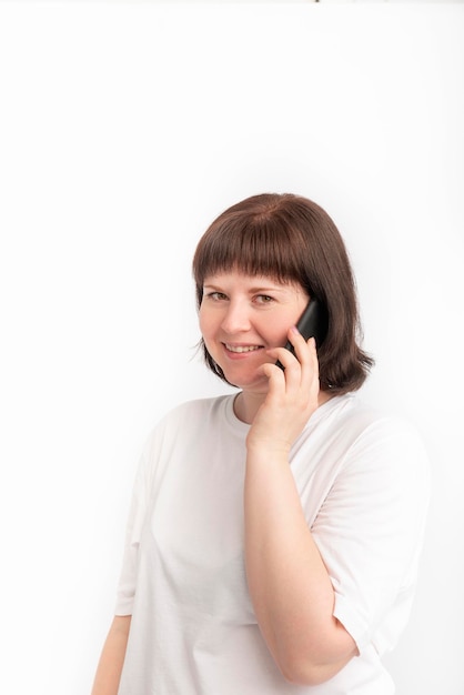 Lächelndes Mädchen, das am Telefon spricht. Porträt der netten rundgesichtigen Frau mit einem Telefon in ihren Händen auf weißem Hintergrund.