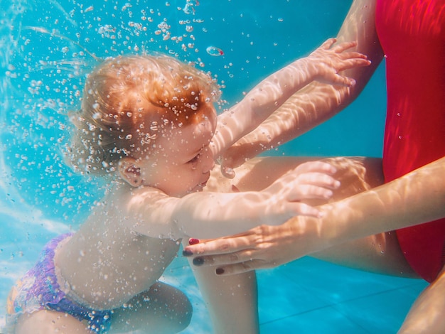 Lächelndes Mädchen, das unter Wasser taucht, blauer Pool Aktiver Lifestyle-Kinderschwimmunterricht mit den Eltern