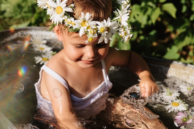 Lächelndes Mädchen des Babys spritzt im Badezimmer, das im Garten steht, an einem heißen sonnigen Sommertag