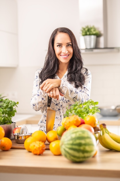 Lächelndes Mädchen hält ein Messer in der Küche, umgeben von frischem Obst und Kräutern.