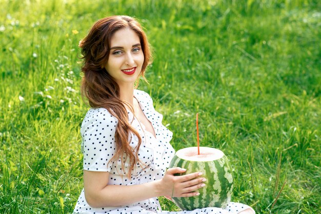 Lächelndes Mädchen hält ganze Wassermelone mit Cocktailstroh auf grünem Hintergrund.