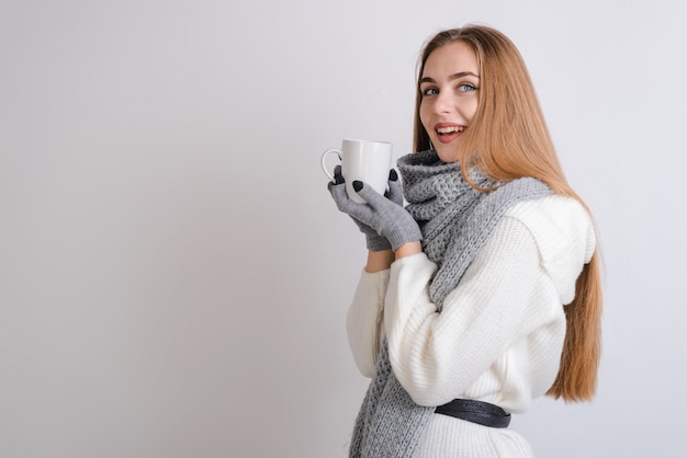 Lächelndes Mädchen im Schal und in den Handschuhen hält Becher in den Händen.