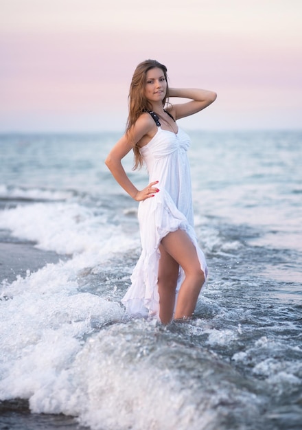 Lächelndes Mädchen im weißen Kleid, das am Strand für ein Foto posiert