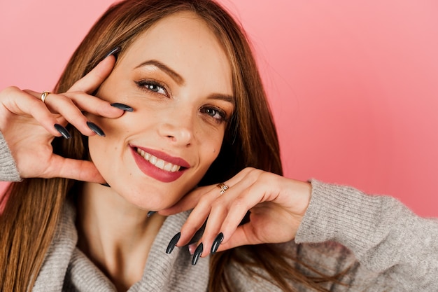 Lächelndes Mädchen in einem grauen Pullover auf einem rosa Hintergrund