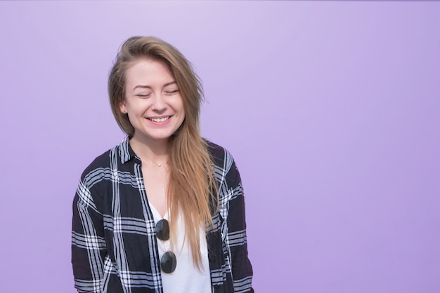 Lächelndes Mädchen in einem Hemd und einem weißen T-Shirt und einem lila Hintergrund.