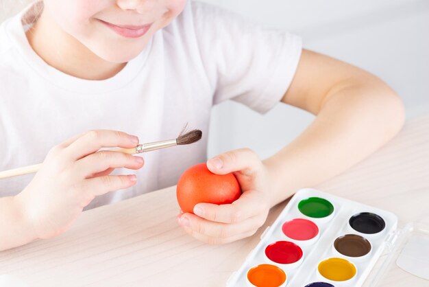 Lächelndes Mädchen malt Ostereier auf einem Holztisch