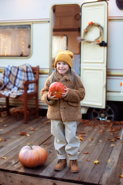 Lächelndes Mädchen mit einem Kürbis in ihren Händen und spielen in der Nähe von Camping im Wohnmobil zu Hause im Herbstgarten