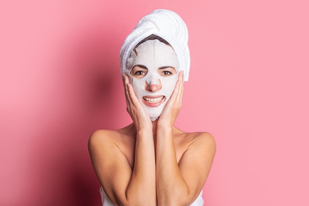 Lächelndes Mädchen mit einer kosmetischen Maske auf ihrem Gesicht auf einem rosafarbenen Hintergrund Spa-Behandlungen