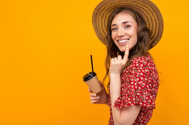 Lächelndes Mädchen mit Kaffee auf gelbem Hintergrund in einem roten Kleid