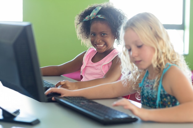 Lächelndes Mädchen mit Klassenkamerad unter Verwendung von Computern