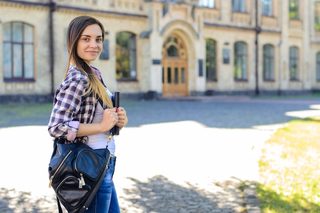 Lächelndes Mädchen mit Rucksack und Buch in der Hand Campus