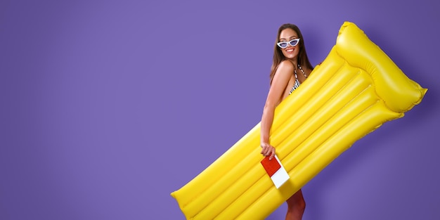 Lächelndes Mädchen mit Sonnenbrille, das aufblasbare Matratze und Tickets mit Reisepass hält