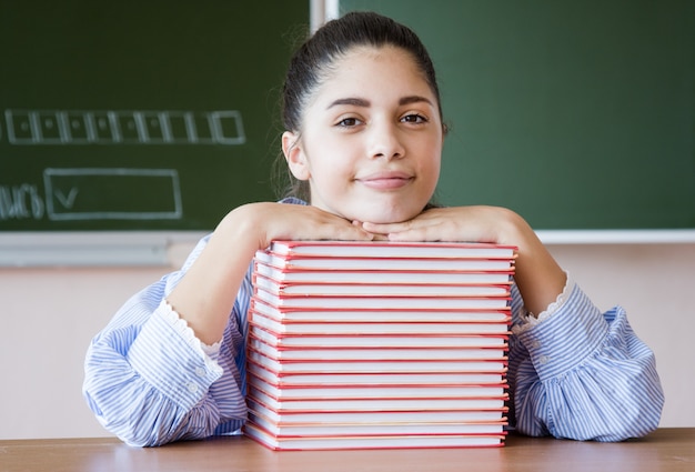 Lächelndes Mädchen sitzt gegen Tafel im Klassenzimmer