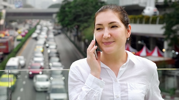 Lächelndes Mädchen spricht auf dem Smartphone, das auf der Brücke auf dem Nahaufnahmeexemplar steht