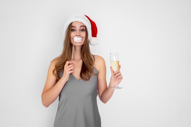 Lächelndes Mädchen trägt Weihnachtsmütze trägt vortäuschen Lächeln hält Glas Champagner Neujahrsparty