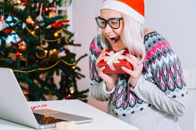 Lächelndes Mädchen zu Hause mit Laptop-Computer-Notebook für Videoanrufe von Freunden und Eltern in Weihnachtsmütze