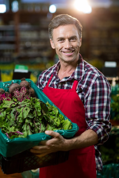 Foto lächelndes männliches personal, das eine kiste frisches gemüse am supermarkt hält