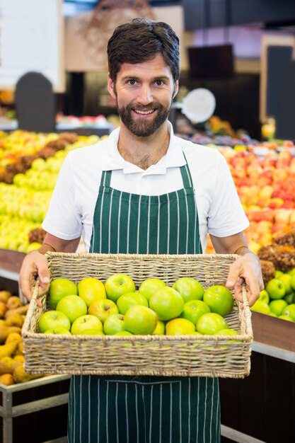 Lächelndes männliches Personal, das einen Korb des grünen Apfels am Supermarkt hält