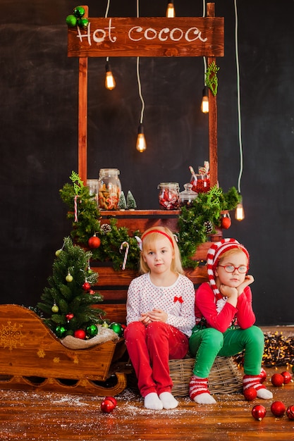 Lächelndes nettes blondes Mädchen und Junge, die auf dem Bretterboden mit Weihnachtsbällen sitzt