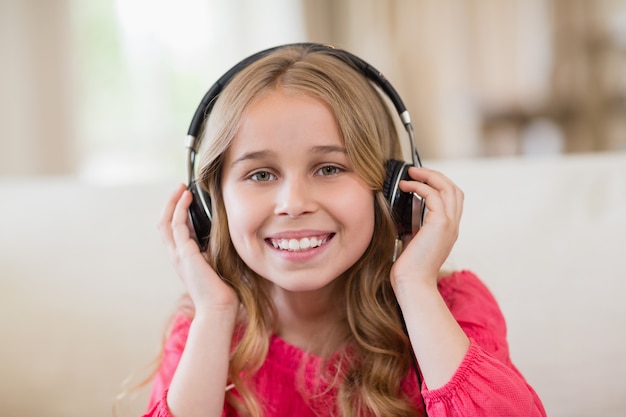 Lächelndes niedliches Mädchen, das Musik auf Kopfhörern im Wohnzimmer zu Hause hört
