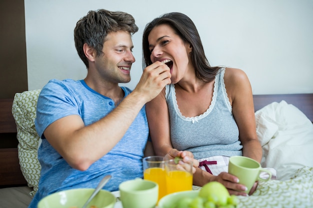 Lächelndes Paar beim Frühstück auf dem Bett