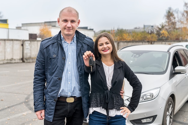 Lächelndes Paar, das nahe neues Auto mit Schlüsseln aufwirft