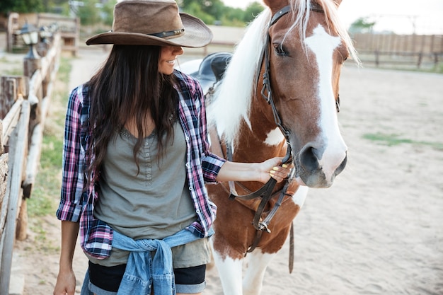 Lächelndes reizendes Cowgirl der jungen Frau mit ihrem Pferd im Dorf