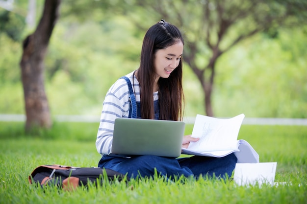 Lächelndes schönes asiatisches Mädchenlesebuch und Arbeiten am Baum auf Park im Sommer für entspannen sich Zeit