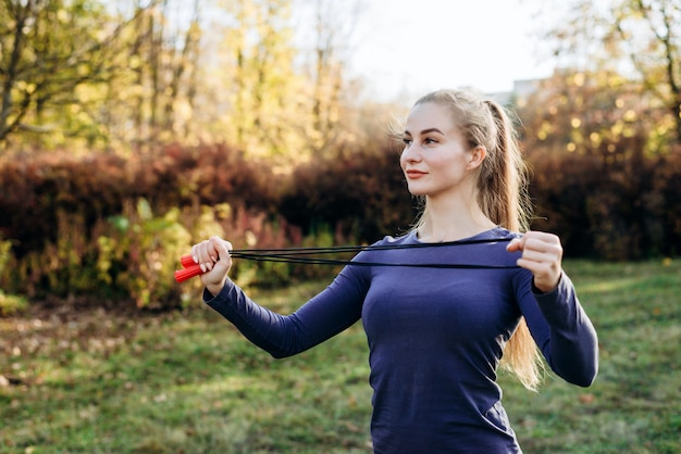 Lächelndes, schönes blondes Mädchen, das Springseil draußen tut