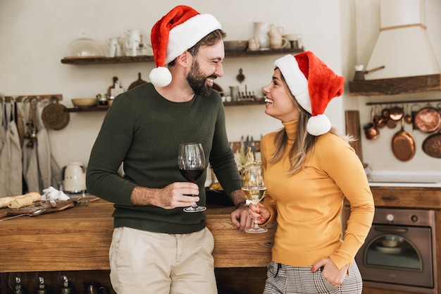 Lächelndes schönes junges Paar, das zusammen Weihnachten feiert, Toasten beim Stehen in der Küche