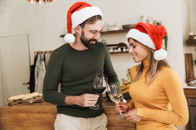 Lächelndes schönes junges Paar, das zusammen Weihnachten feiert, Toasten beim Stehen in der Küche