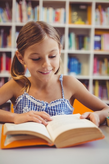 Lächelndes Schulmädchen, das ein Buch in der Bibliothek liest