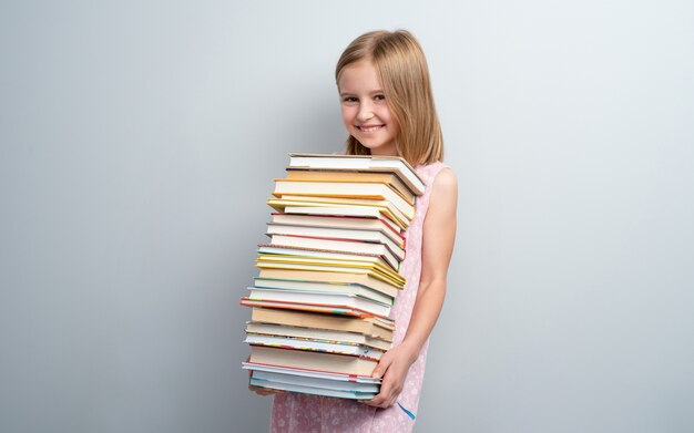 Lächelndes Schulmädchen, das Stapel Bücher lokalisiert hält