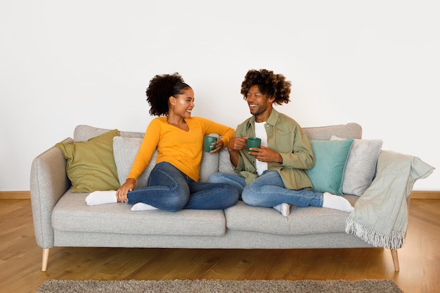 Lächelndes schwarzes Paar auf der Couch, Kaffee trinkend und Gespräche drinnen genießend