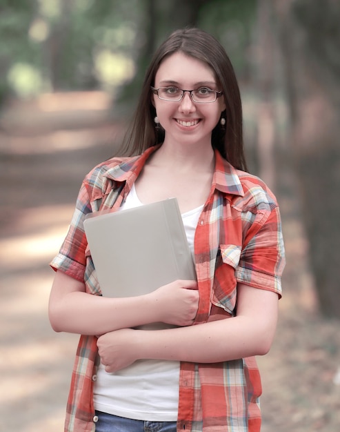 Lächelndes Studentenmädchen mit einer Zwischenablage auf dem Hintergrund des Parks.