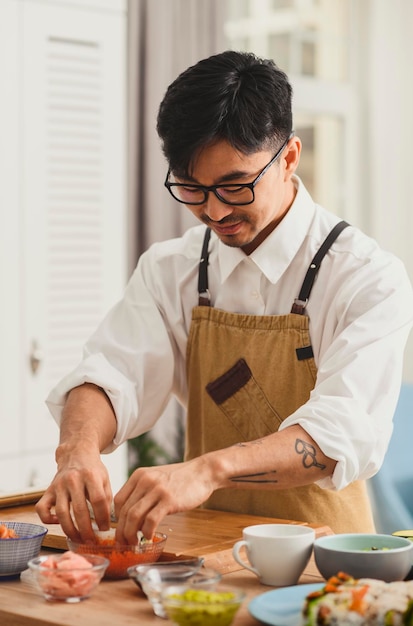 Foto lächelndes sushi-meisterporträt bei der arbeit stillleben männlicher koch macht sushi und brötchen aus reis